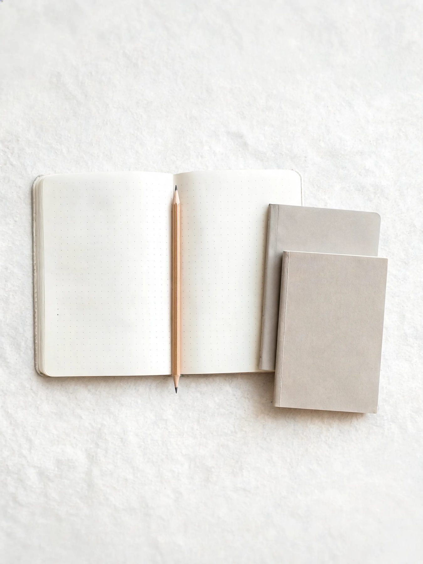 Open dotted notebook with a graphite pencil and two pocket books stacked beside it